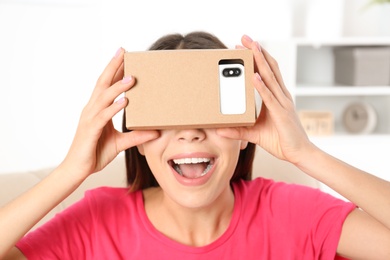 Photo of Young woman using cardboard virtual reality headset at home