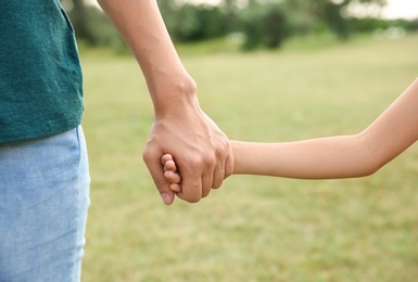 Photo of Woman holding hands with her child outdoors, closeup. Happy family