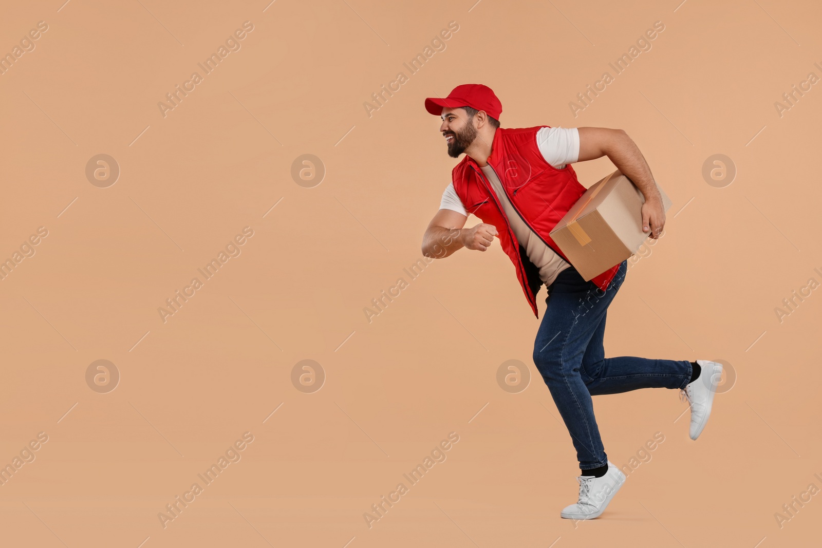Photo of Happy courier running to deliver parcel on light brown background, space for text
