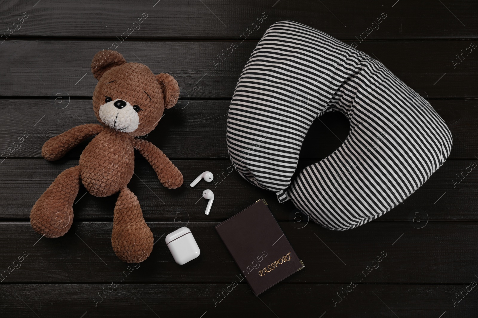 Photo of Striped travel pillow, toy bear, passport and earphones on dark wooden background, flat lay