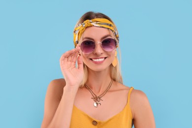 Photo of Portrait of smiling hippie woman in sunglasses on light blue background