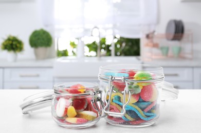 Image of Glass jars with tasty gummy candies on white table in kitchen. Space for text