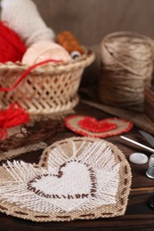 Photo of Heart shaped pieces of burlap fabric with different stitches and sewing tools on wooden table, closeup