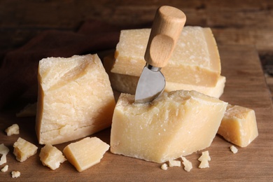 Photo of Parmesan cheese with knife on wooden board, closeup
