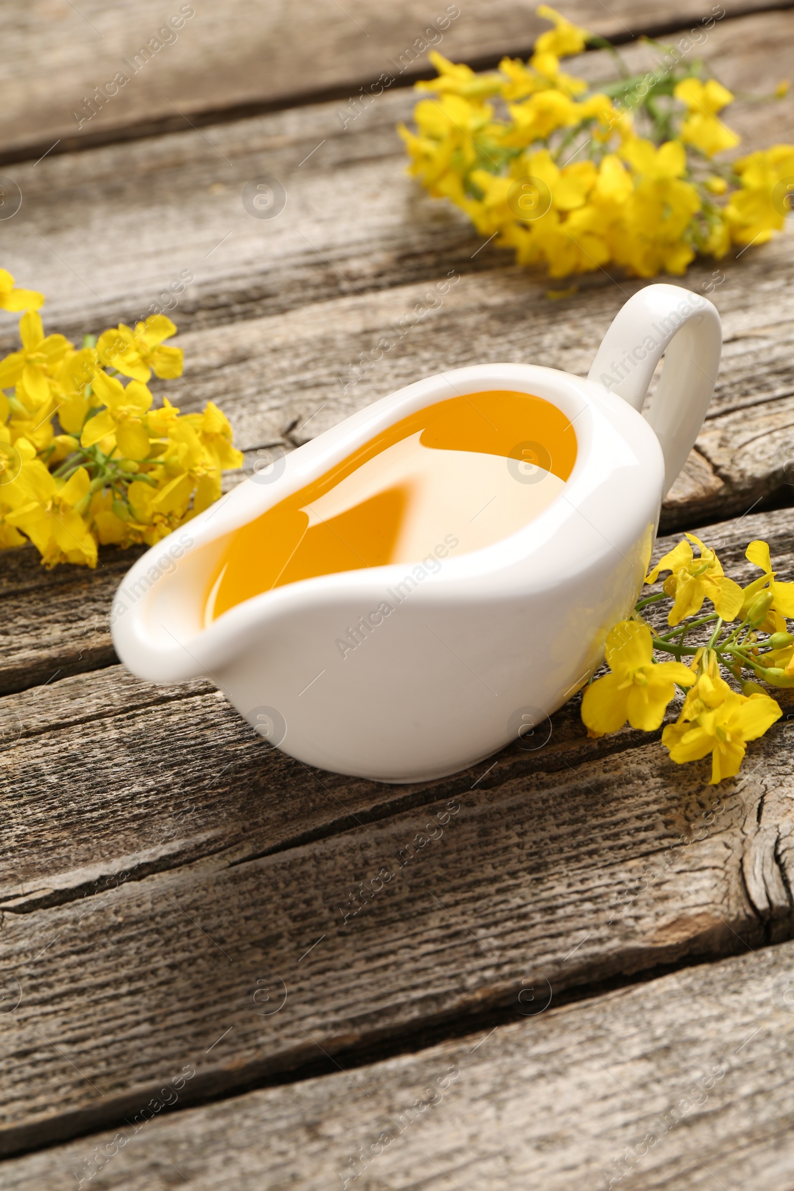 Photo of Rapeseed oil in gravy boat and beautiful yellow flowers on wooden table