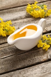 Photo of Rapeseed oil in gravy boat and beautiful yellow flowers on wooden table