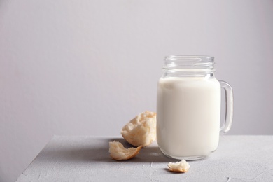 Photo of Mason jar with milk and bun pieces on table against grey wall