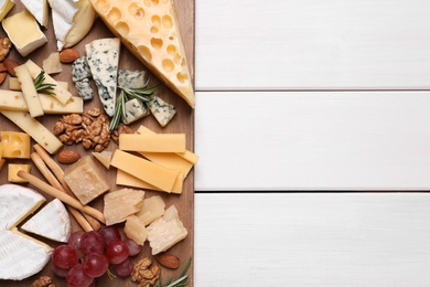 Photo of Cheese plate with grapes and nuts on white wooden table, top view. Space for text
