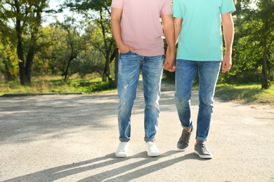 Photo of Gay couple with wristbands holding hands outdoors. Space for text