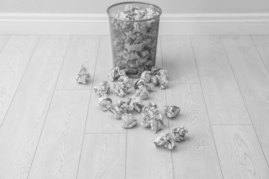 Metal bin and crumpled paper on floor near light wall