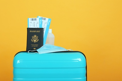 Photo of Passport with tickets, sanitizer and protective mask on suitcase against yellow background, space for text. Travel during quarantine