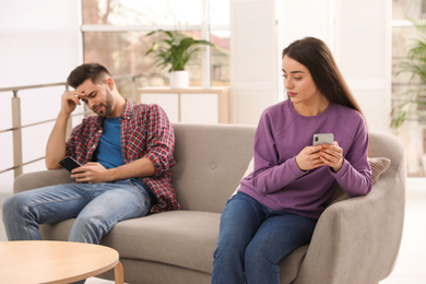 Photo of Young couple preferring smartphones over spending time together on couch at home
