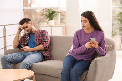 Young couple preferring smartphones over spending time together on couch at home