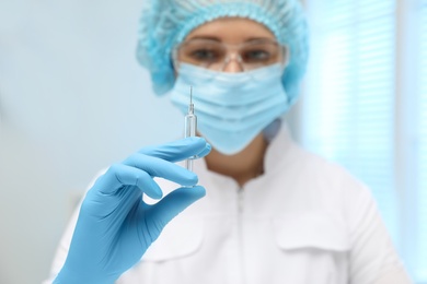 Doctor holding syringe with COVID-19 vaccine on blurred background