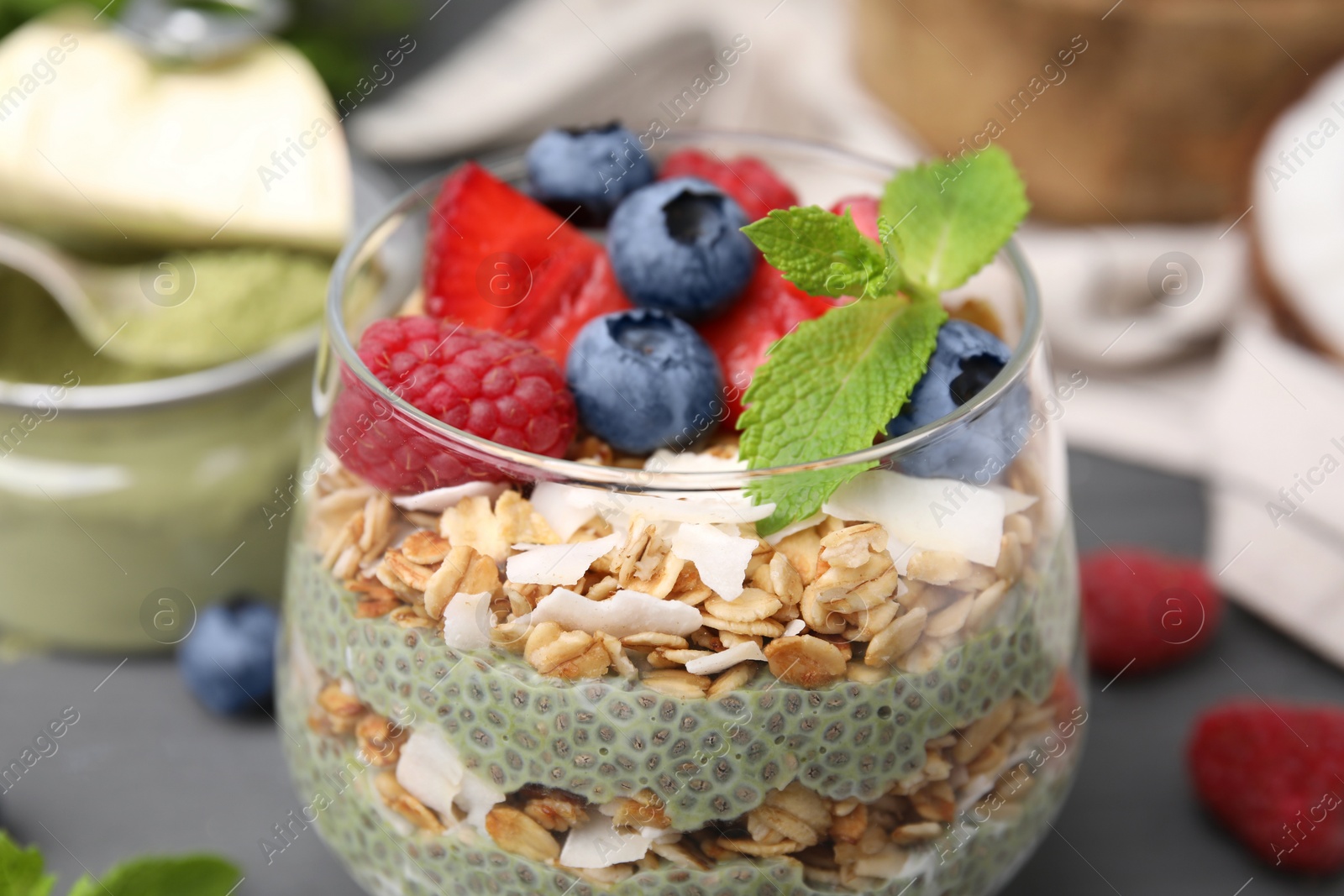 Photo of Tasty oatmeal with chia matcha pudding and berries on black wooden table, closeup. Healthy breakfast