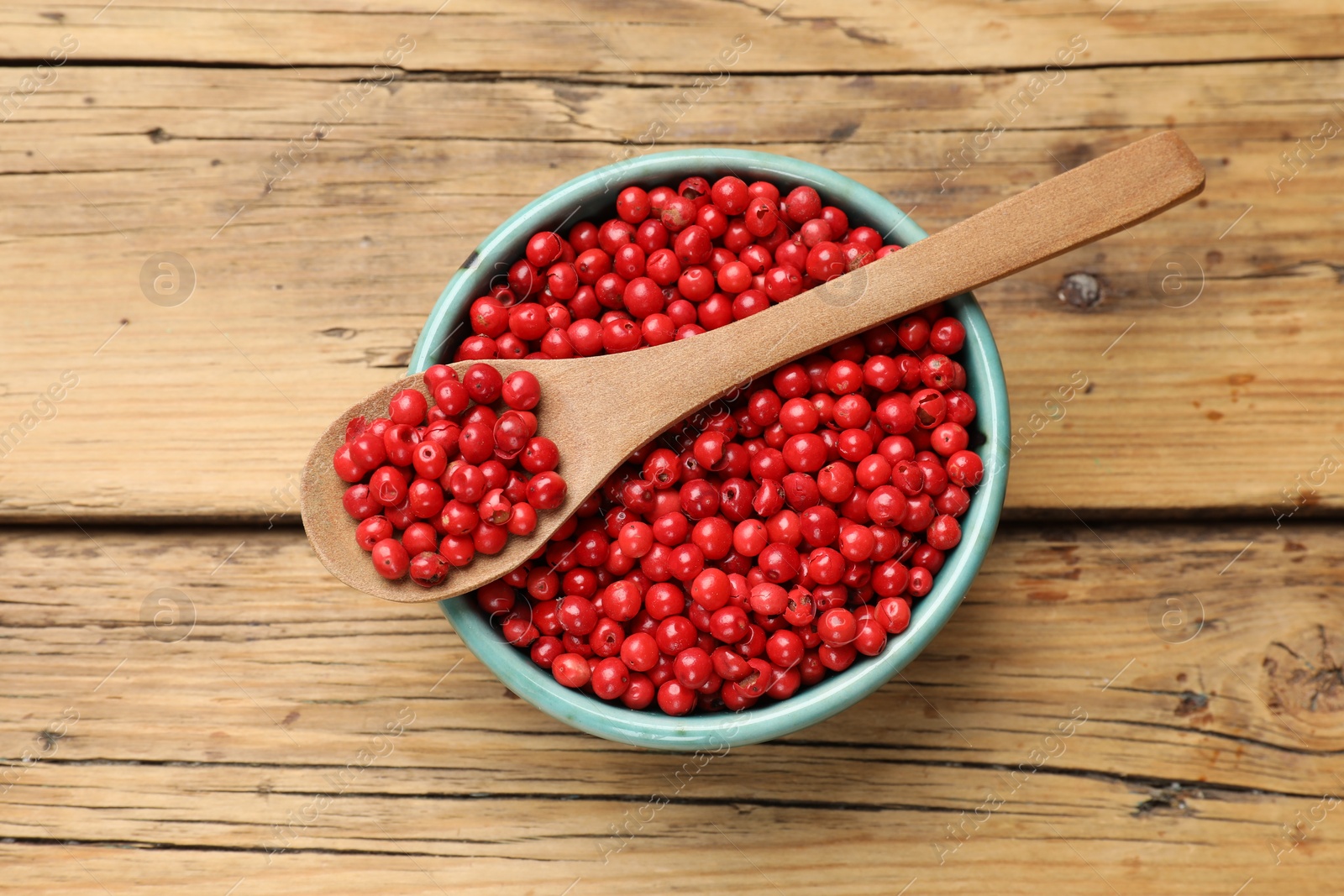 Photo of Aromatic spice. Red pepper in bowl and spoon on wooden table, top view