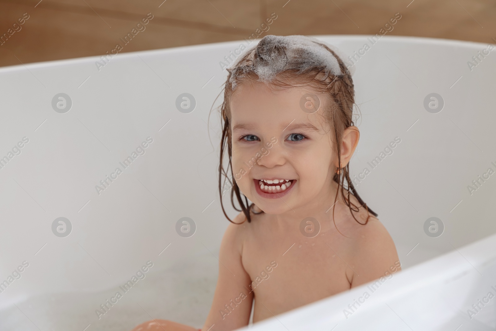 Photo of Cute little girl washing hair with shampoo in bathroom