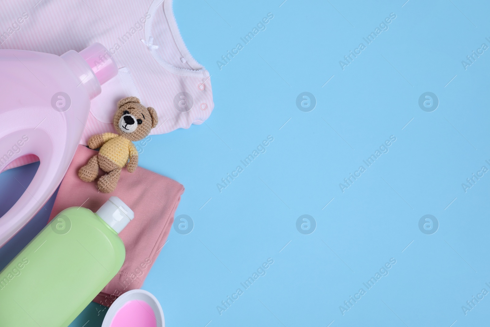 Photo of Laundry detergents, baby clothes and toy bear on light blue background, flat lay. Space for text