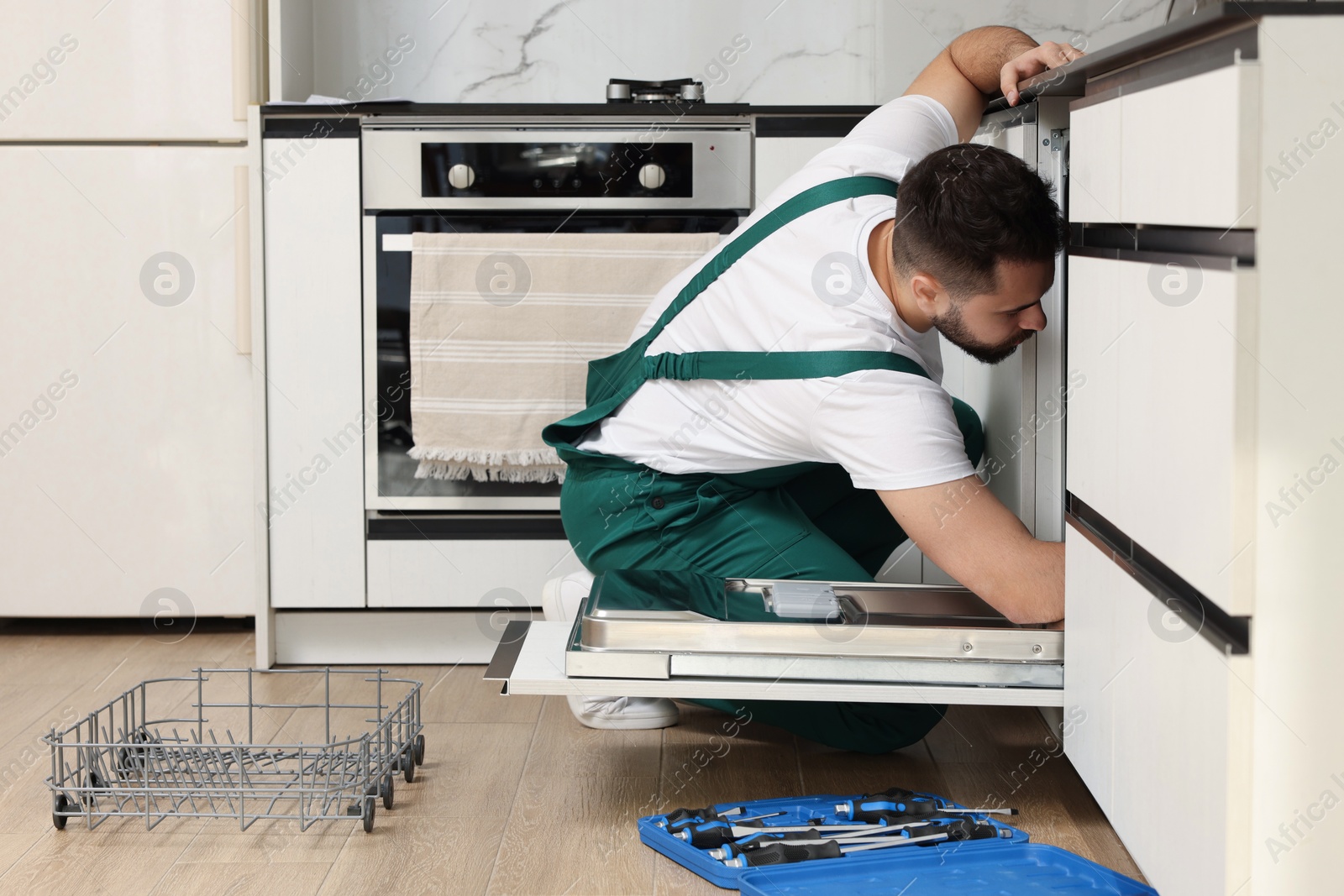 Photo of Serviceman repairing dishwasher near toolbox in kitchen