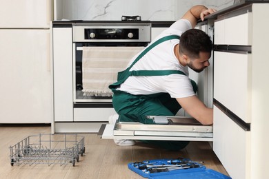 Serviceman repairing dishwasher near toolbox in kitchen