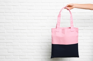 Young woman holding textile bag near white brick wall, closeup. Space for text