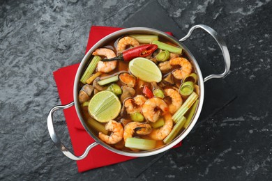 Saucepan with delicious Tom Yum soup on black marble table, top view