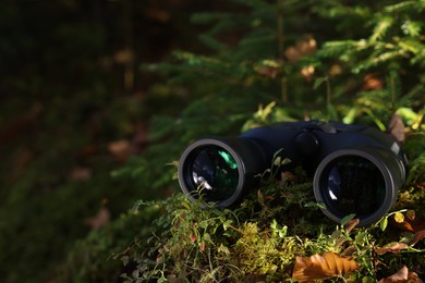 Modern binoculars on ground overgrown with moss, space for text