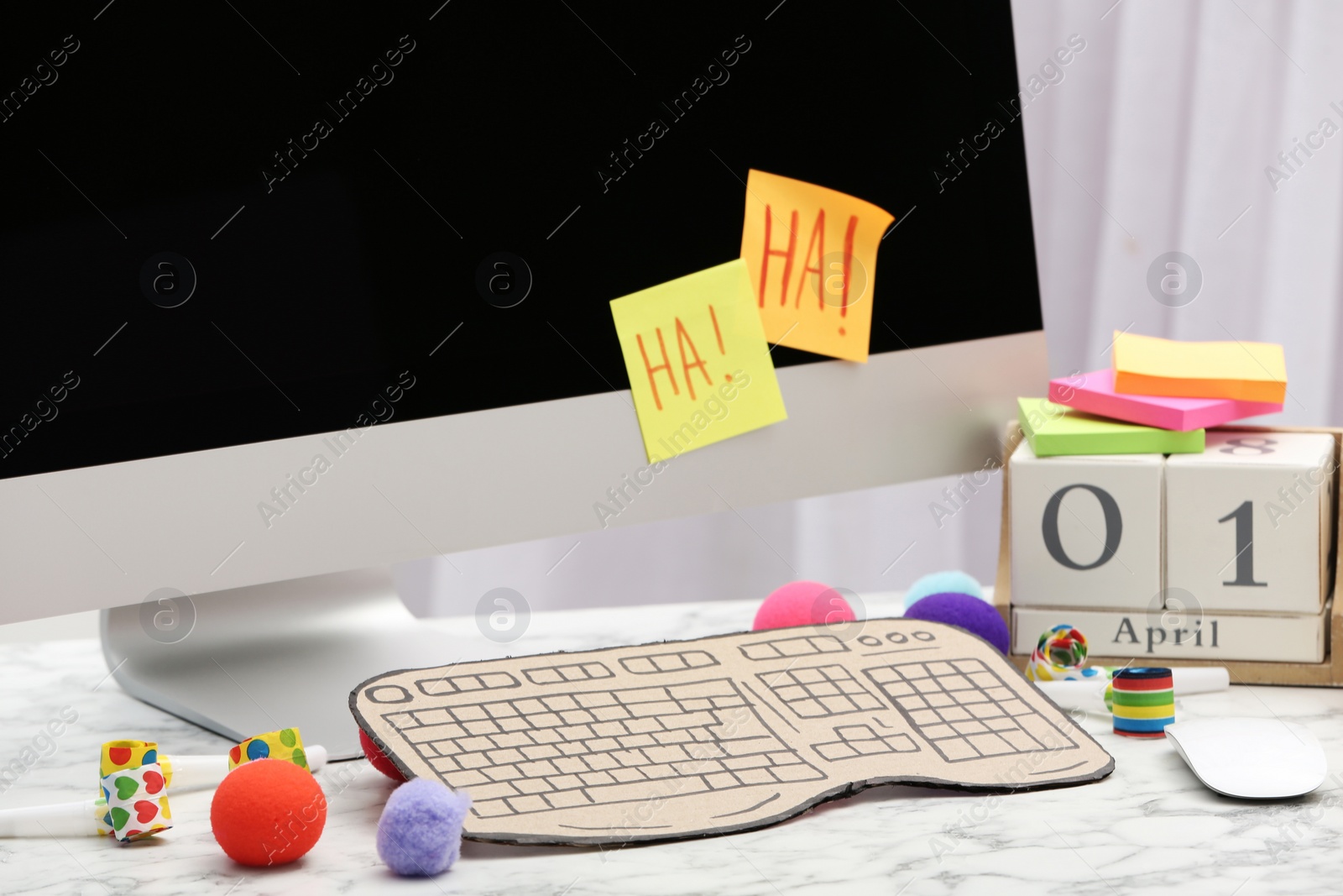 Photo of Computer with cardboard keyboard on white marble table. April Fool's Day