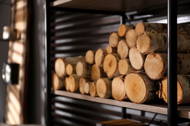 Shelving unit with stacked firewood near wall in room, closeup. Idea for interior design