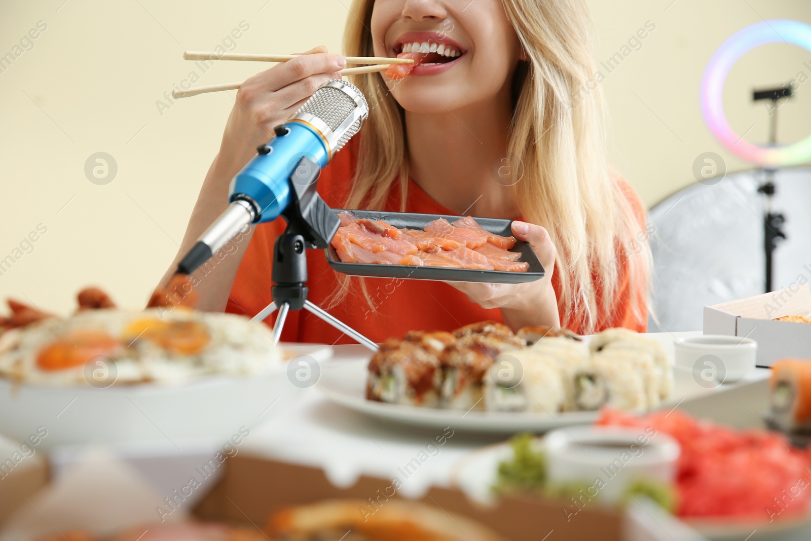 Photo of Food blogger eating in front of microphone at table against light background, closeup. Mukbang vlog