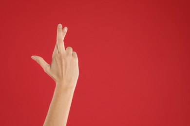 Woman with crossed fingers and space for text on red background, closeup. Superstition concept