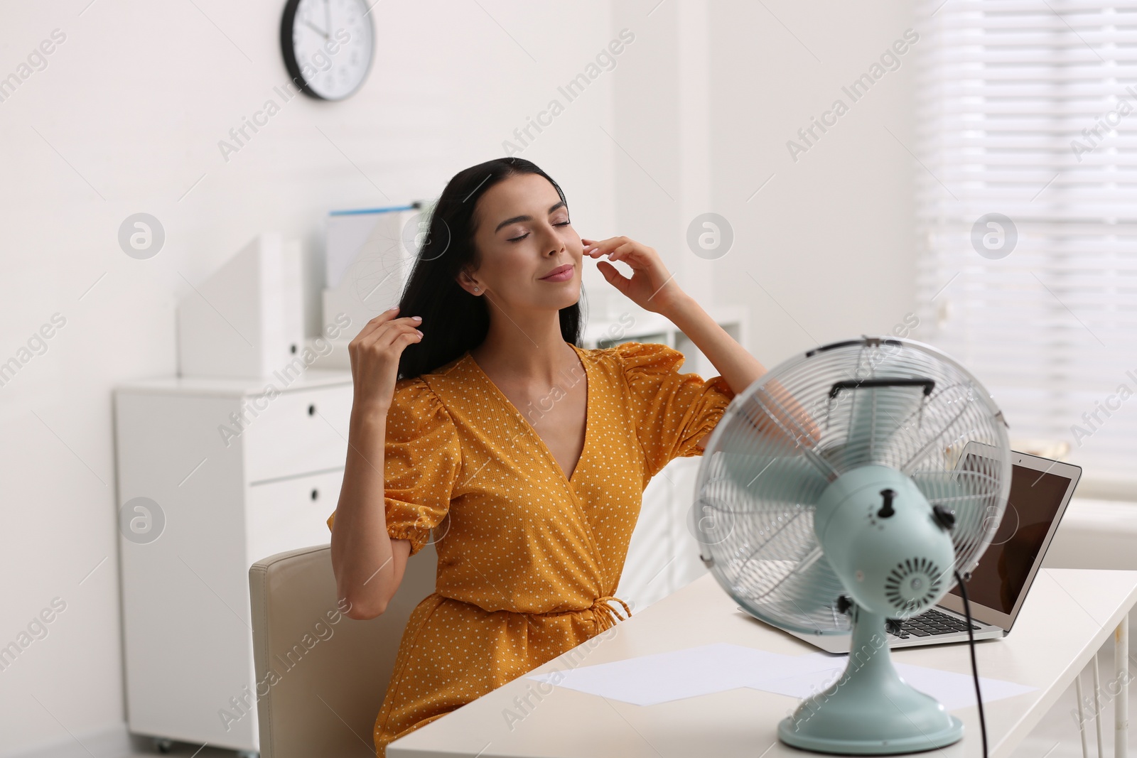 Photo of Young woman enjoying air flow from fan at workplace