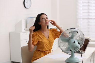 Photo of Young woman enjoying air flow from fan at workplace