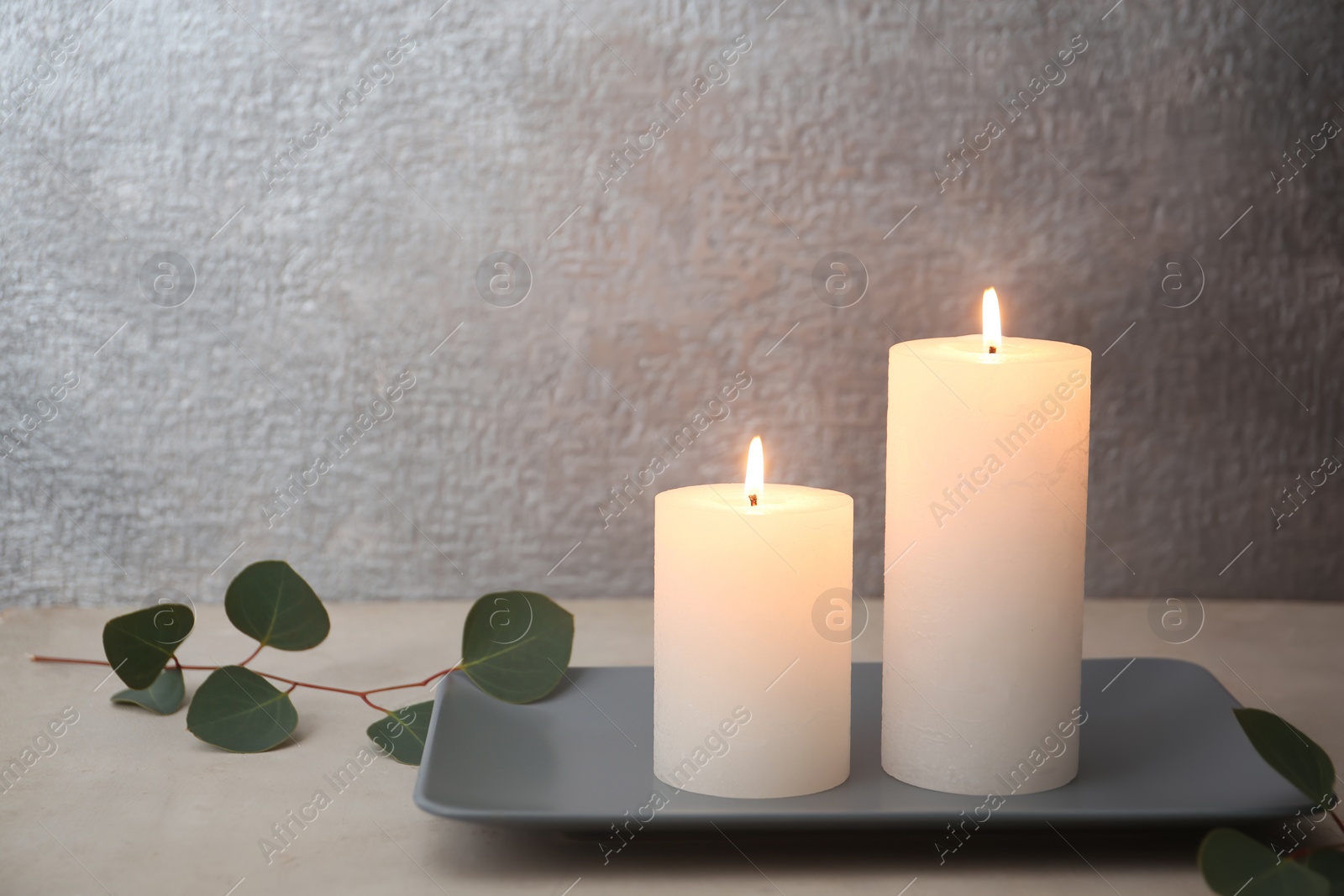 Photo of Candles with floral decor on table against color background