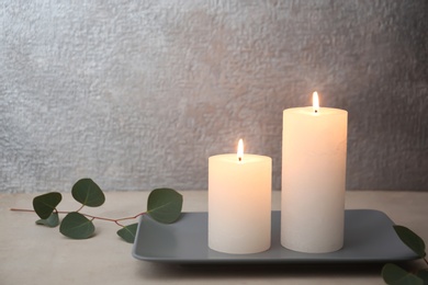 Photo of Candles with floral decor on table against color background