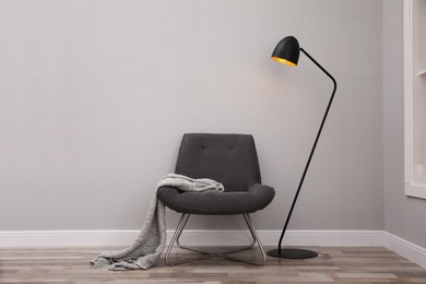 Photo of Comfortable armchair with blanket and lamp near grey wall indoors