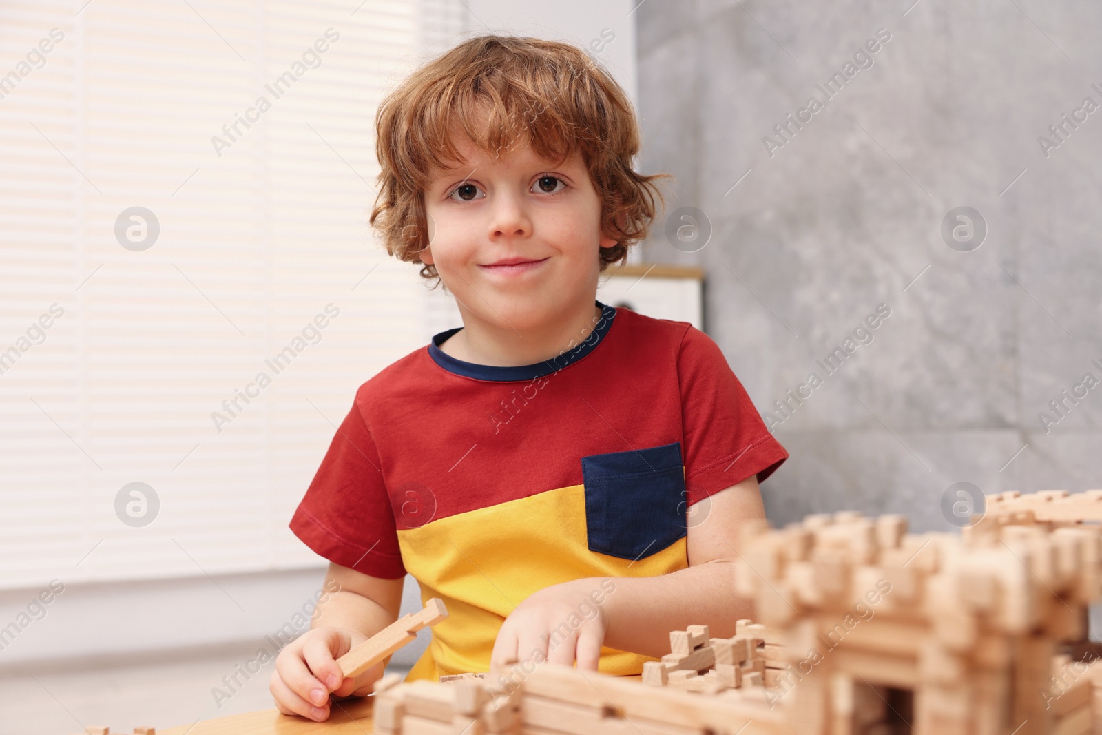 Photo of Little boy playing with wooden entry gate at table in room. Child's toy