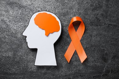 Photo of Human head cutout, brain and orange ribbon on grey table, flat lay. Multiple sclerosis concept