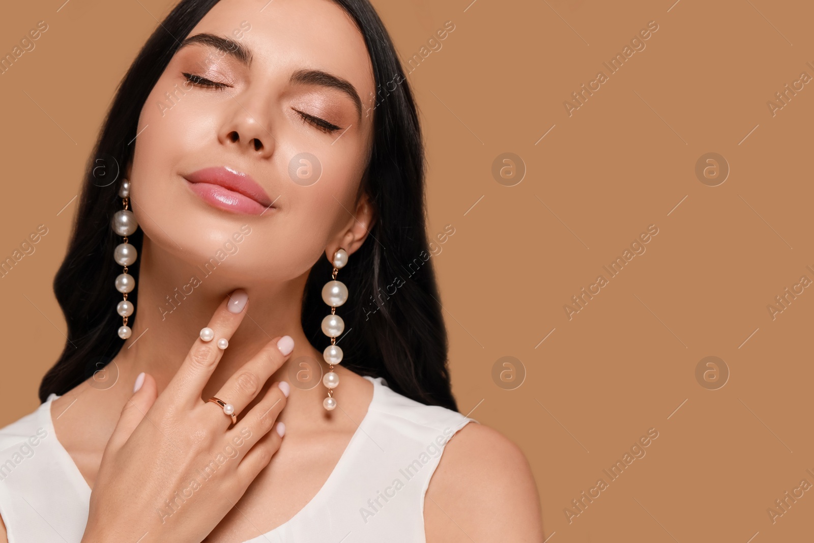 Photo of Young woman wearing elegant pearl jewelry on brown background, space for text