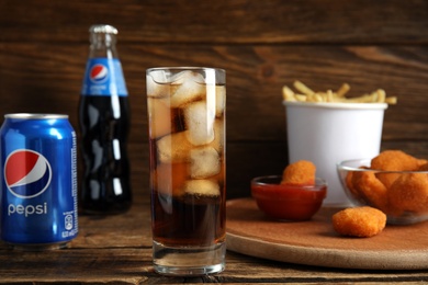 Photo of MYKOLAIV, UKRAINE - FEBRUARY 15, 2021: Glass of Pepsi, can and snacks on wooden table