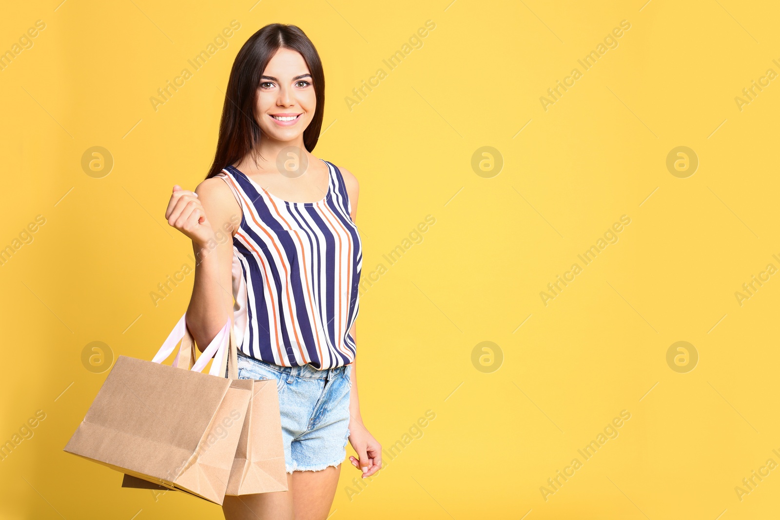 Photo of Portrait of young woman with paper bags on yellow background, space for text