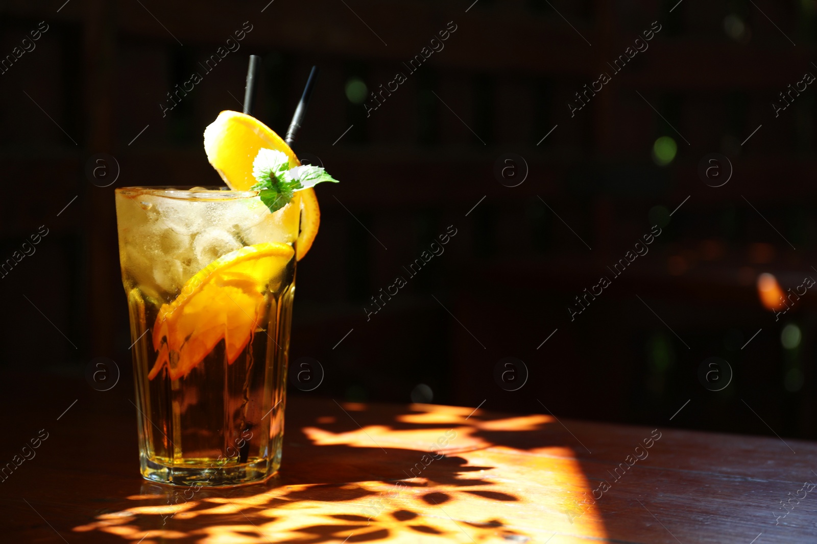 Photo of Glass of delicious cocktail with ice on table in darkness