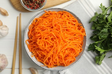 Photo of Delicious Korean carrot salad, garlic, parsley and spices on white wooden table, flat lay