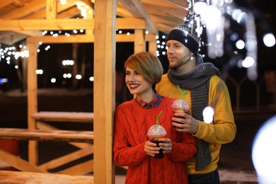 Photo of Young couple with cups of mulled wine at winter fair. Space for text
