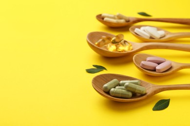 Photo of Different vitamin pills in spoons and green leaves on yellow background, closeup. Space for text