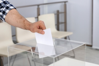 Man putting his vote into ballot box at polling station, closeup. Space for text