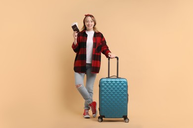 Photo of Happy young woman with passport, ticket and suitcase on beige background