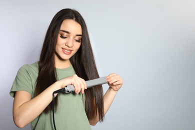 Photo of Happy woman using hair iron on grey background. Space for text