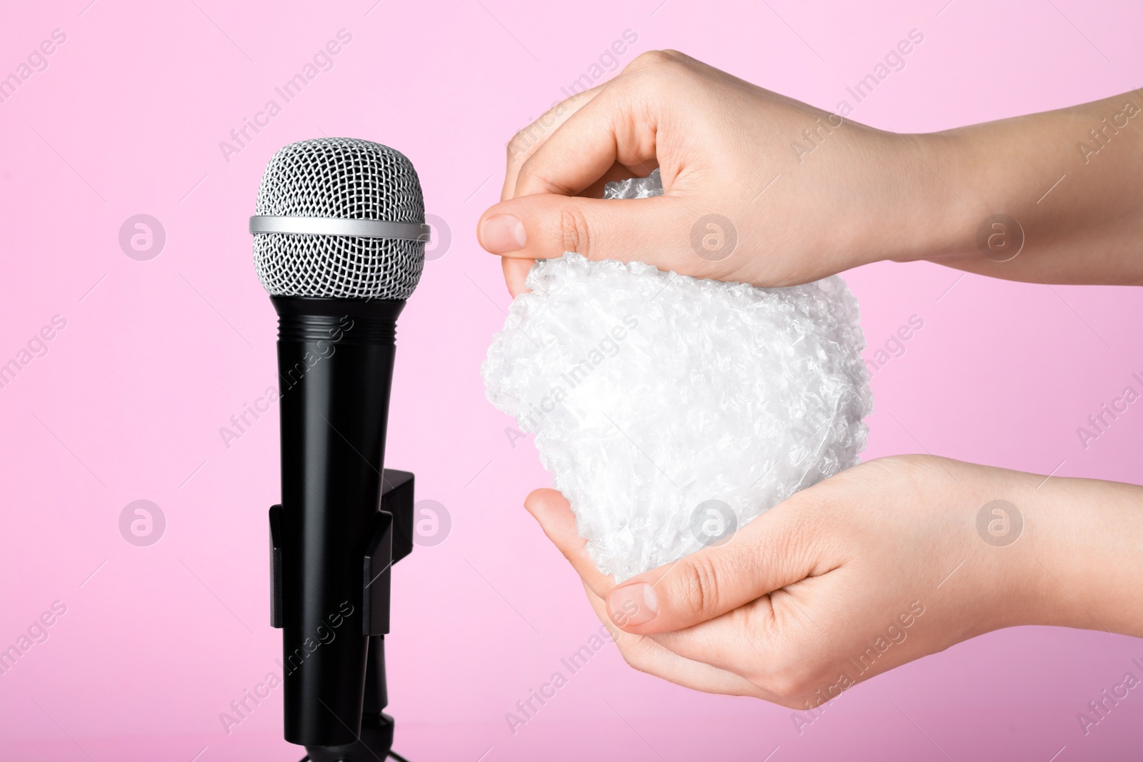 Photo of Woman making ASMR sounds with microphone and bubble wrap on pink background, closeup