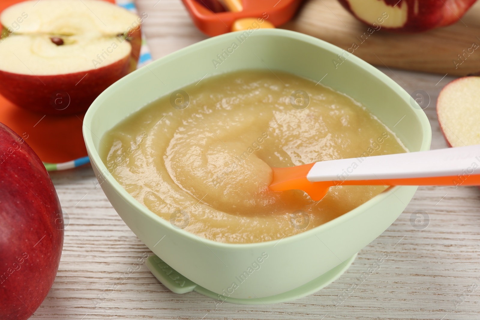 Photo of Healthy baby food. Bowl with delicious apple puree and fresh fruits on white wooden table, closeup